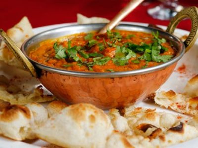 Delicious Indian curry garnished with cilantro served with naan in a copper dish.